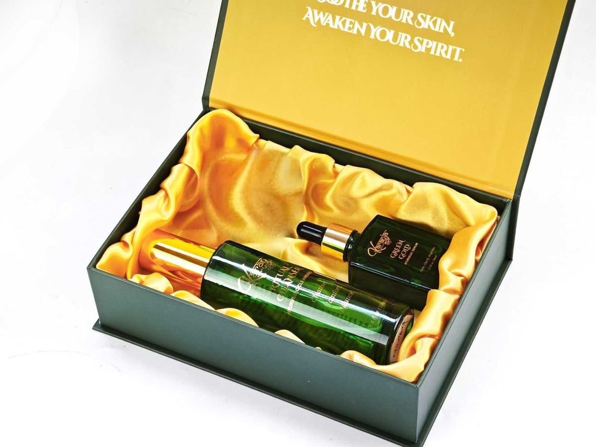 The Karanja Ritual gift box, open, holding the Ritual Cleanser, Green Gold Serum and Shanti Barrier Balm on gold satin.
